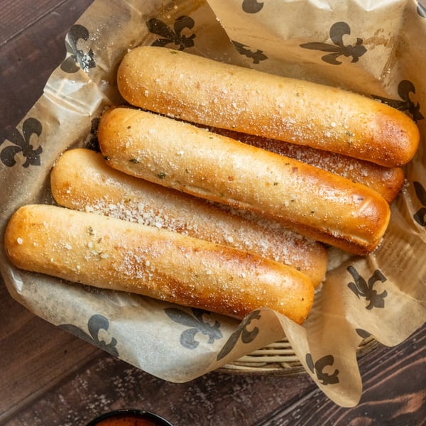 Alesi Pizza House breadsticks, sprinkled with Parmesan cheese and herbs, in a basket lined with branded paper.