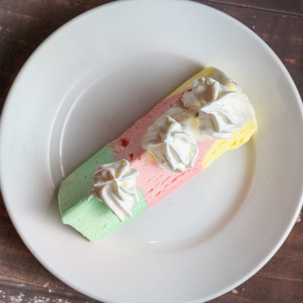 Alesi Pizza House's colorful spumoni ice cream dessert with whipped cream on a white plate.