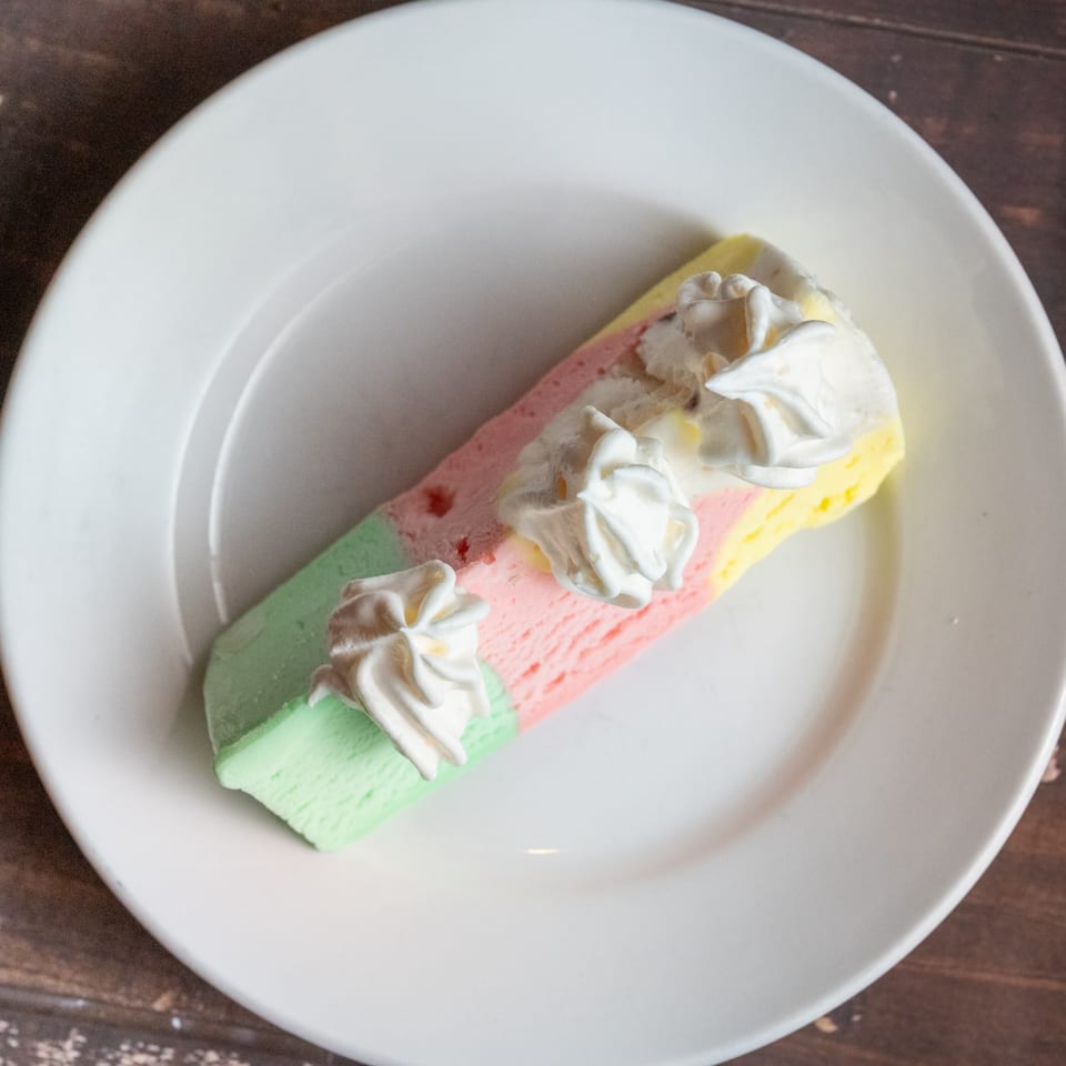Alesi Pizza House's colorful spumoni ice cream dessert with whipped cream on a white plate.