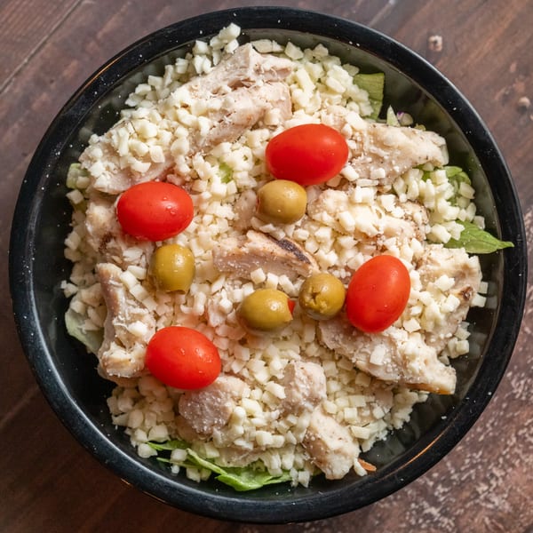 Alesi Pizza House's Italian salad with chicken, cheese, cherry tomatoes, and green olives in a black bowl.