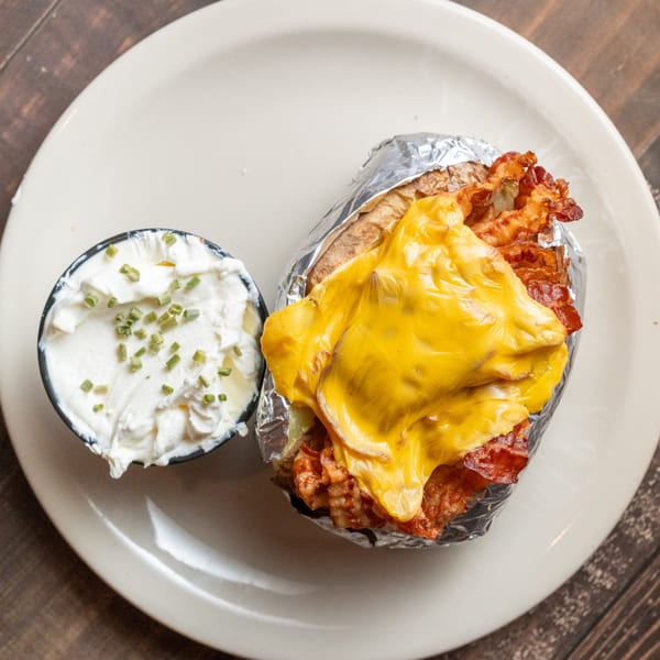 A loaded baked potato with melted cheese, bacon, and a side of sour cream with chives.