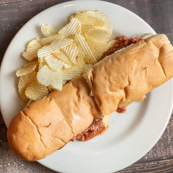 Alesi Pizza House meatball sub with chips on a white plate, shot from above.